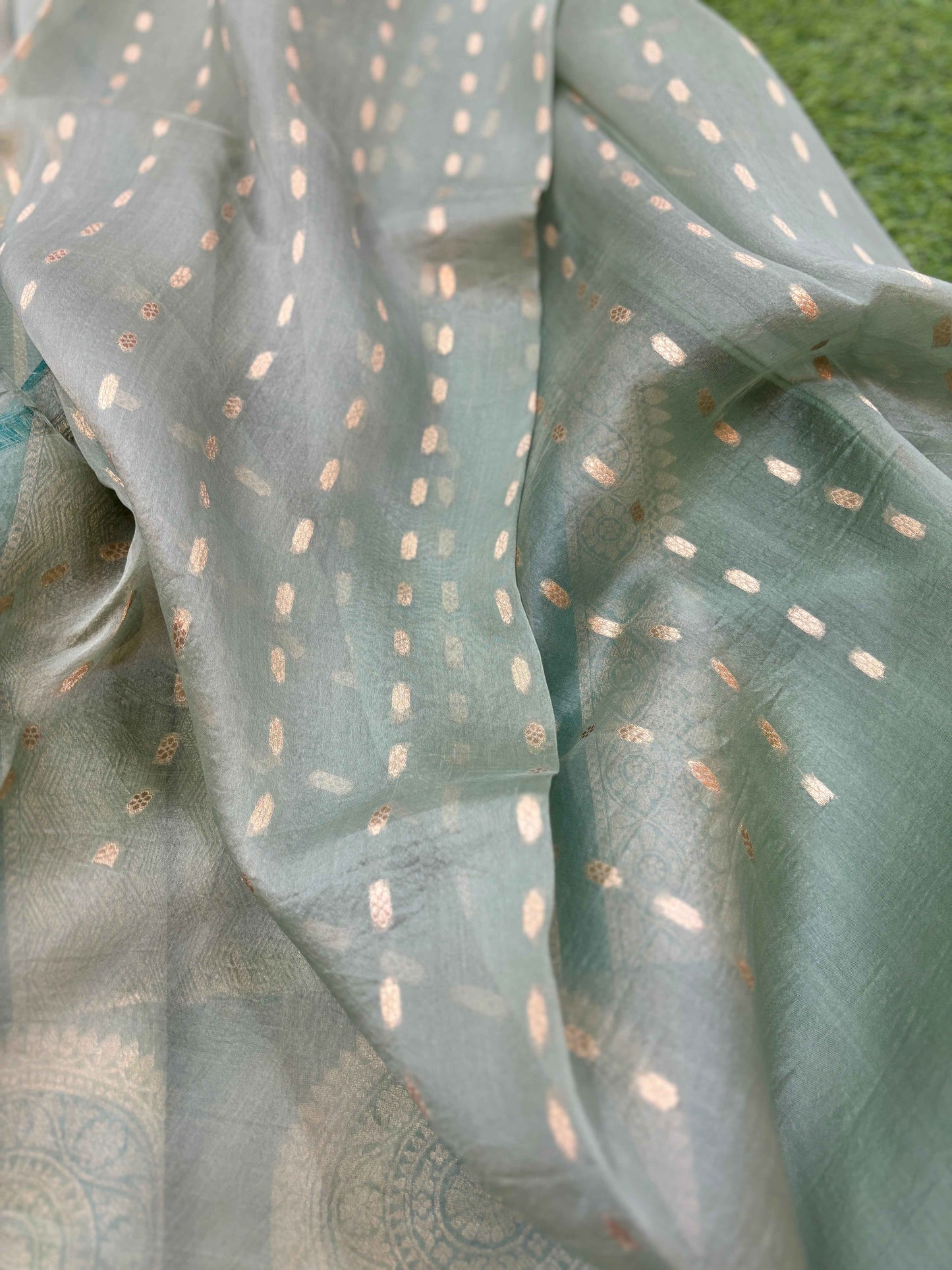 Light blue saree with teal edge, scattered gold dots, and subtle woven medallion