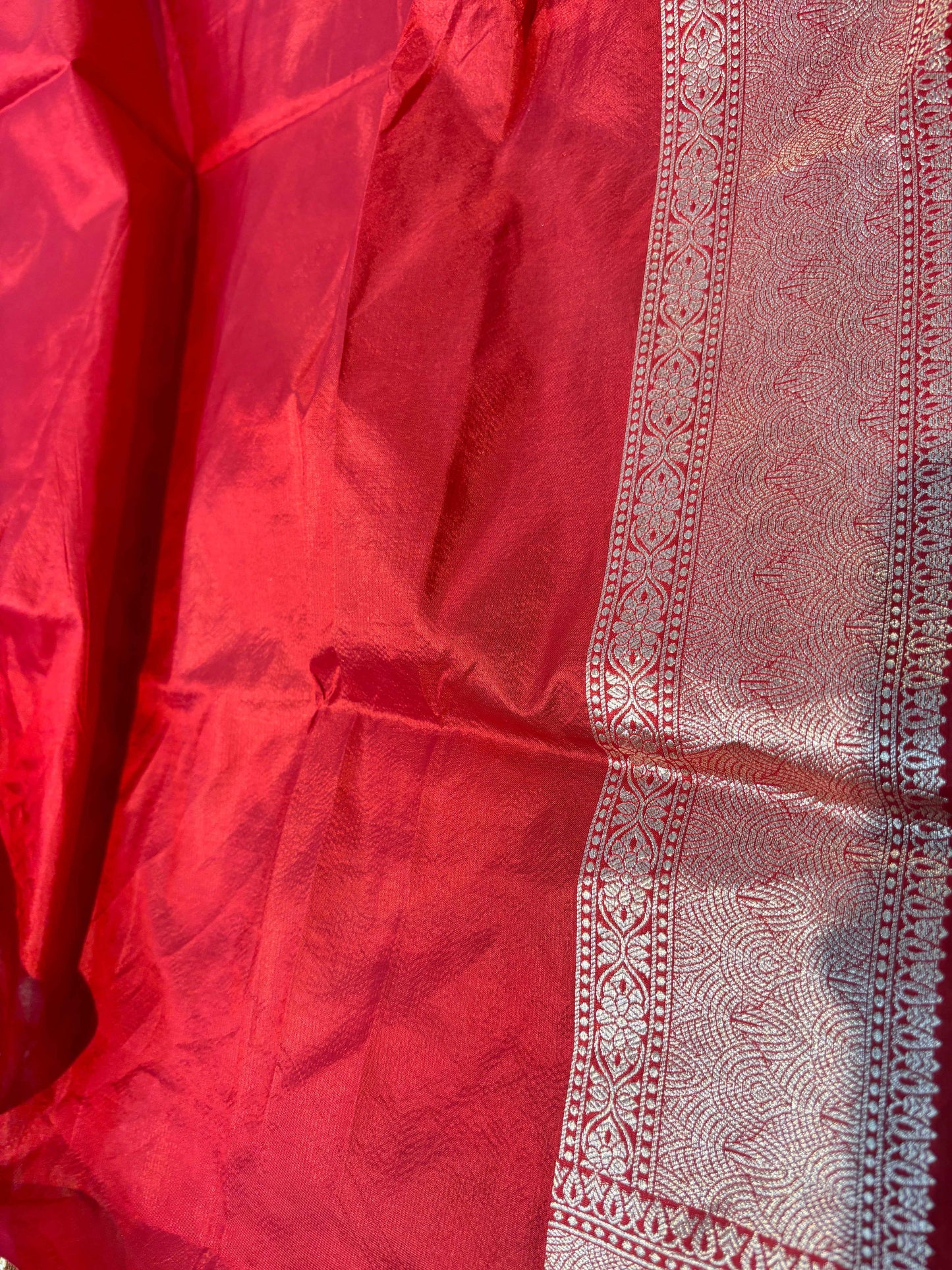 Red saree fabric close-up with ornate rose-gold patterned border panel