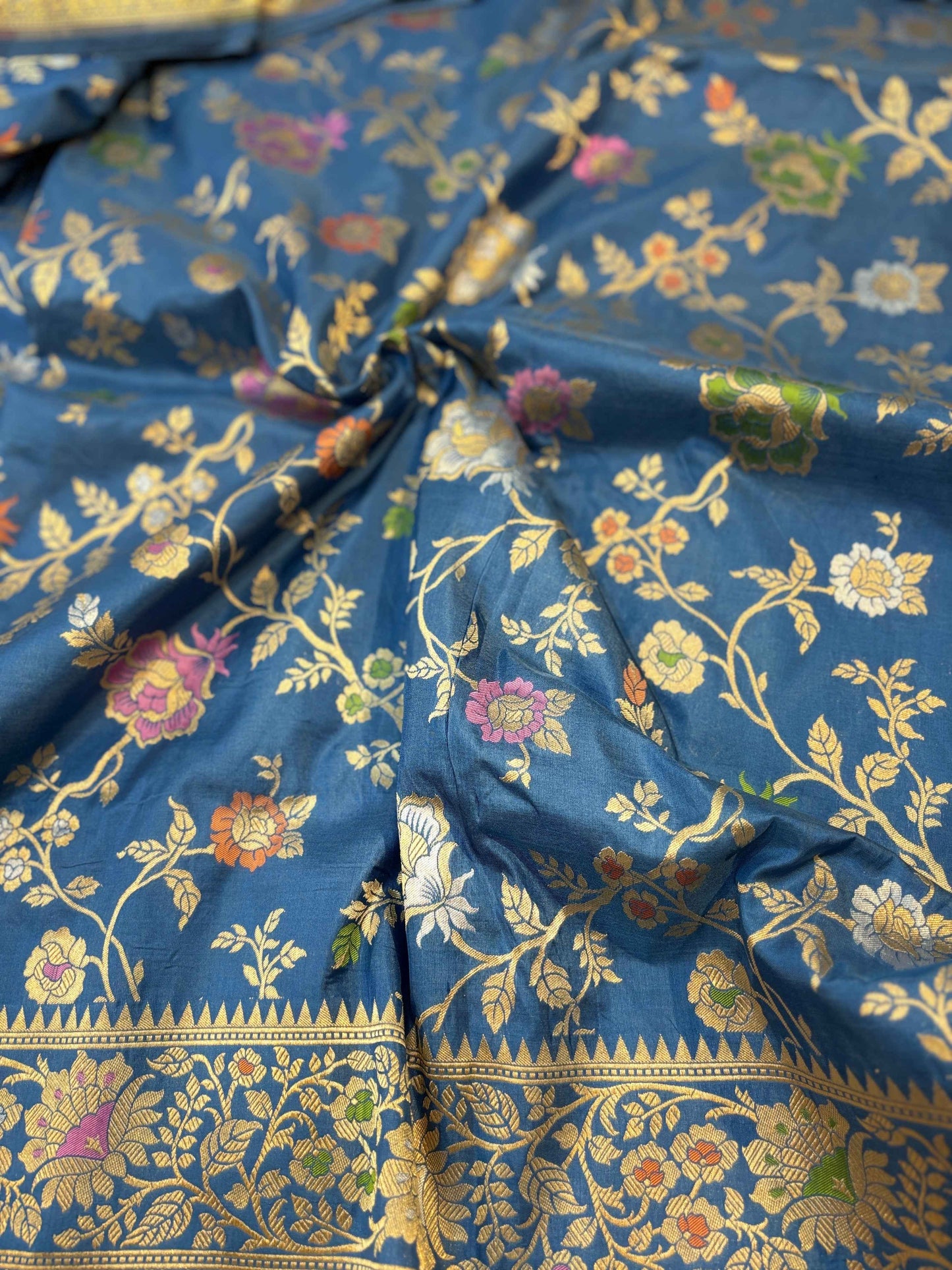 Blue Banarasi handloom saree close-up with gold floral vines and multicolor flowers