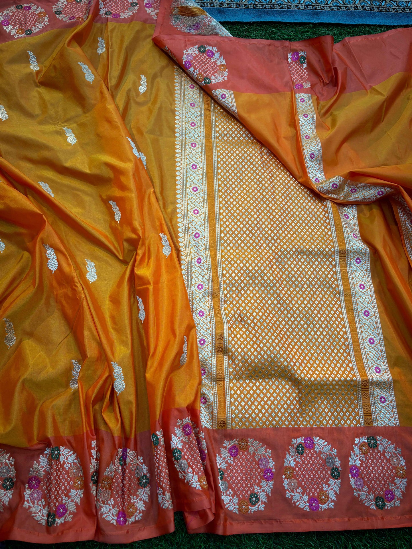 Orange saree with gold motifs, checkered panel, and magenta floral border trim