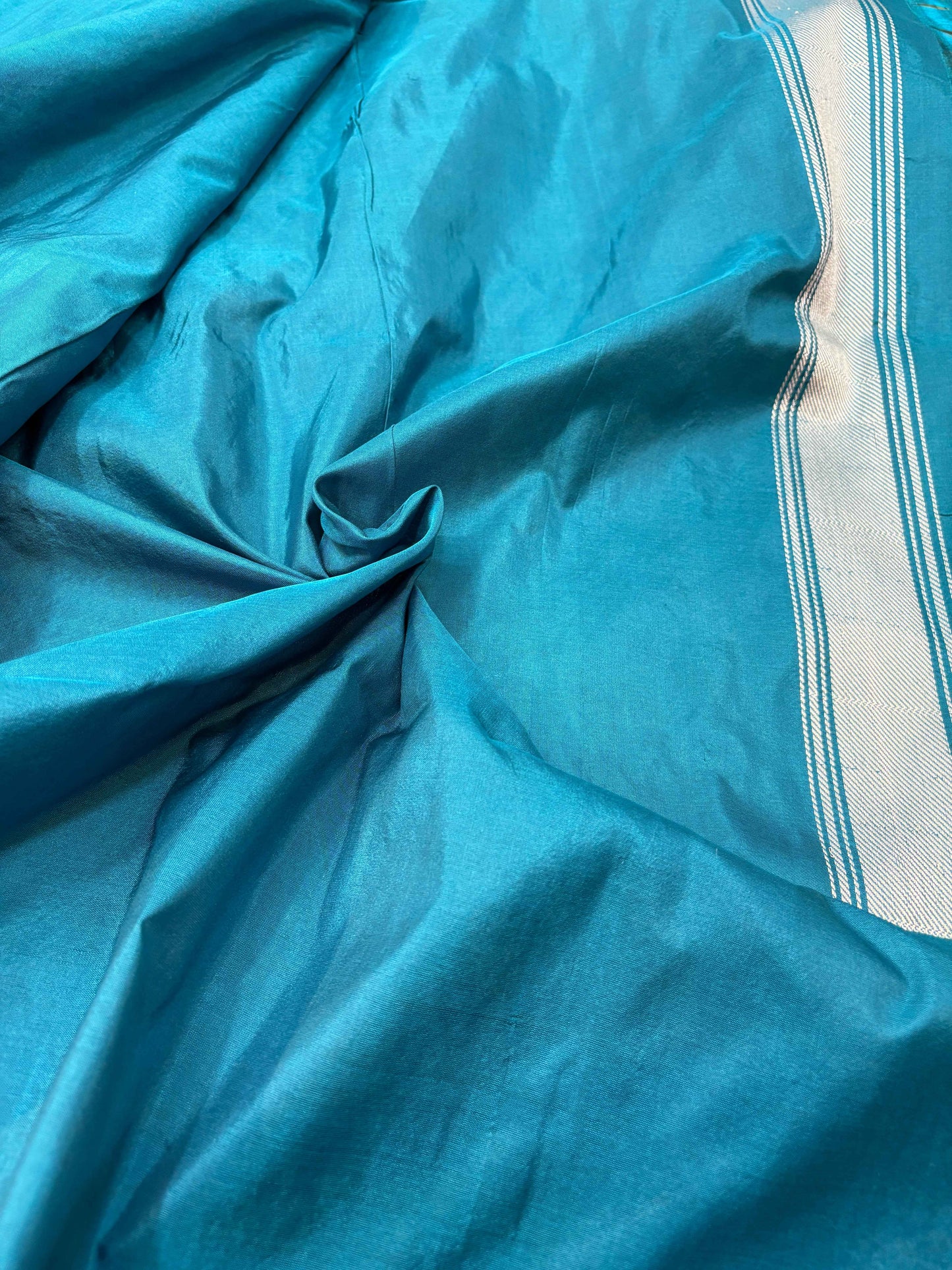 Teal Banarasi saree fabric with pale striped edge and subtle woven texture