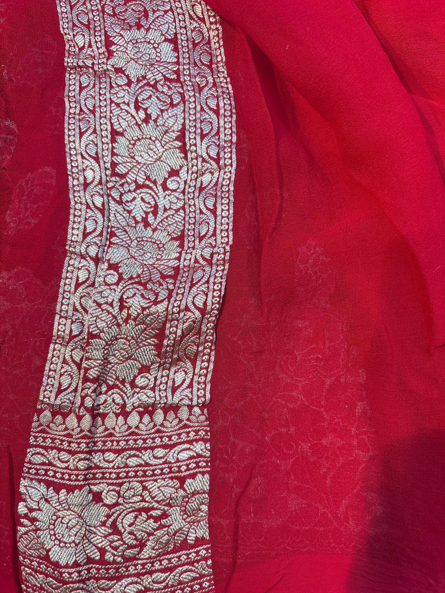 Red saree with vertical embroidered panel and wide ornate silvery border along the edge