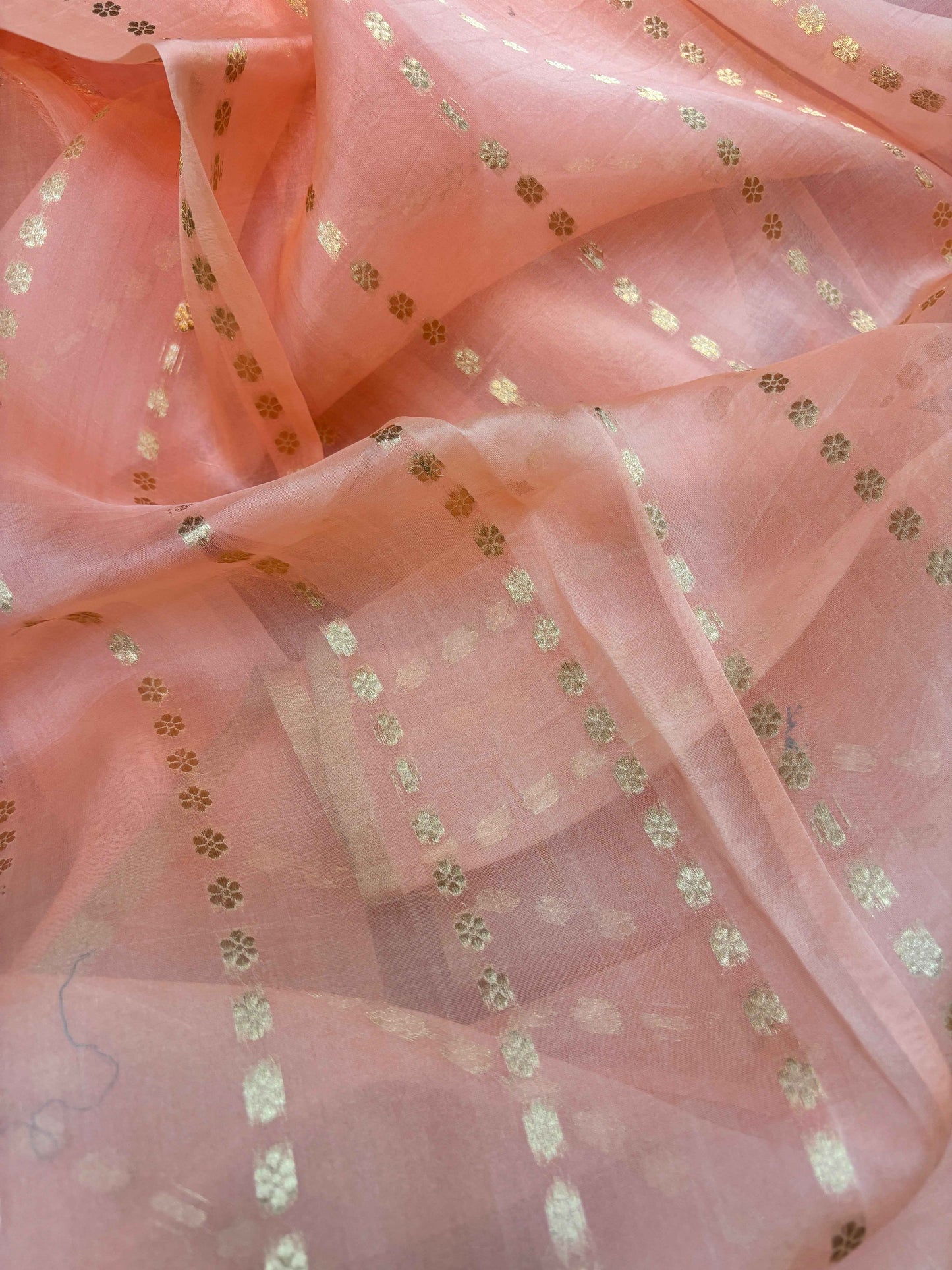 Peach saree fabric with small gold floral dots and subtle sheen, close-up
