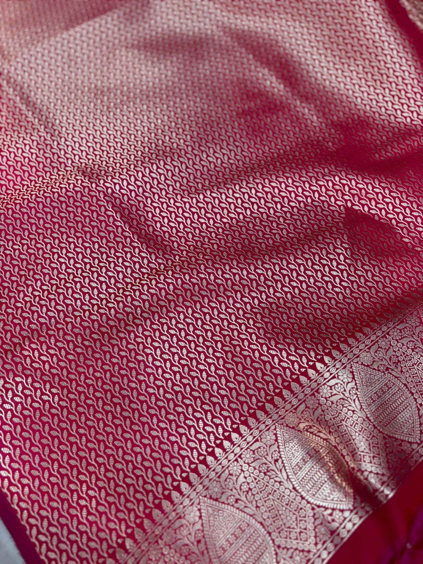 Red textured silk saree fabric close-up with gold woven border and motif work