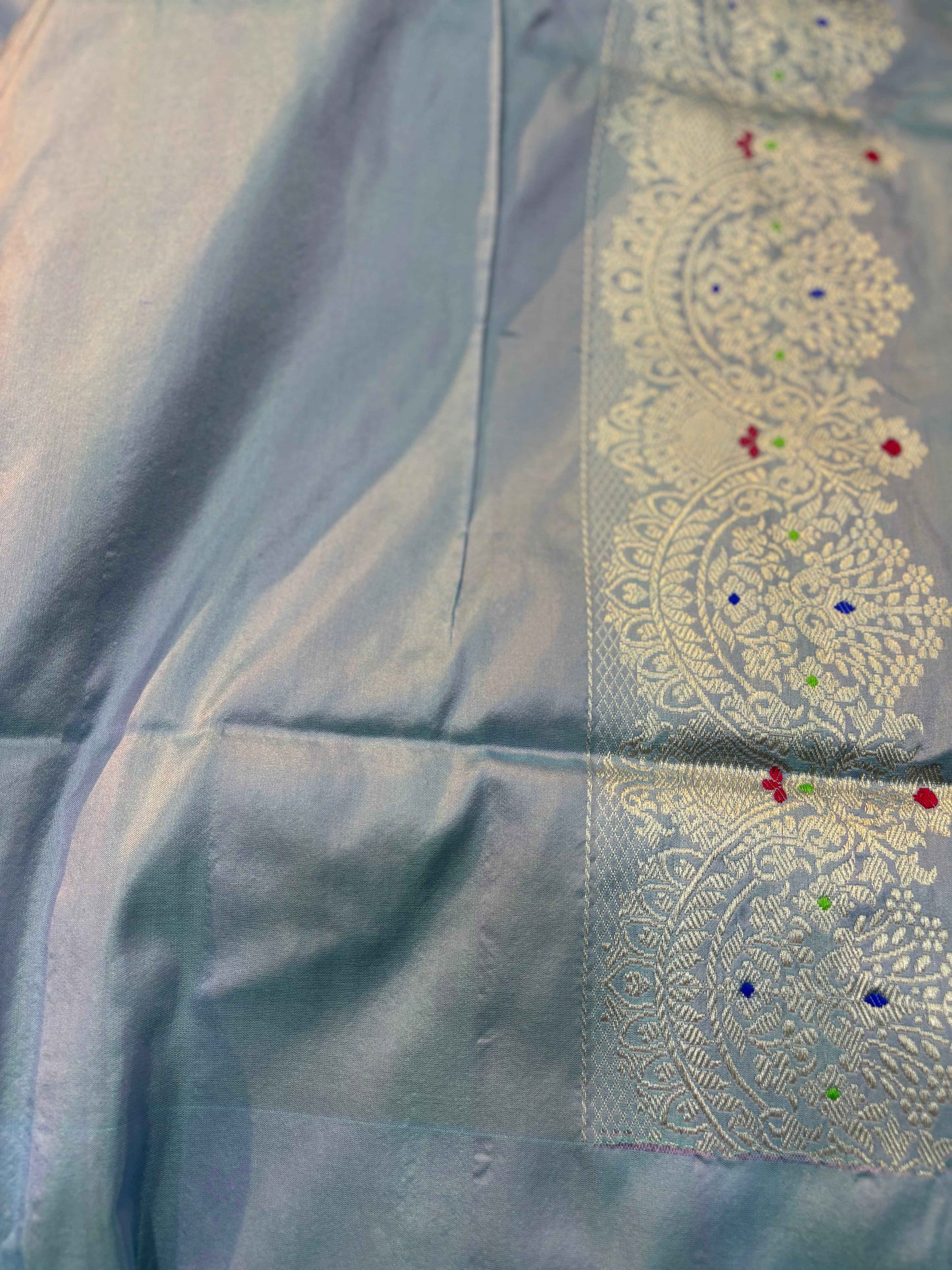 Saree fabric close-up with light blue sheen and embroidered floral medallion