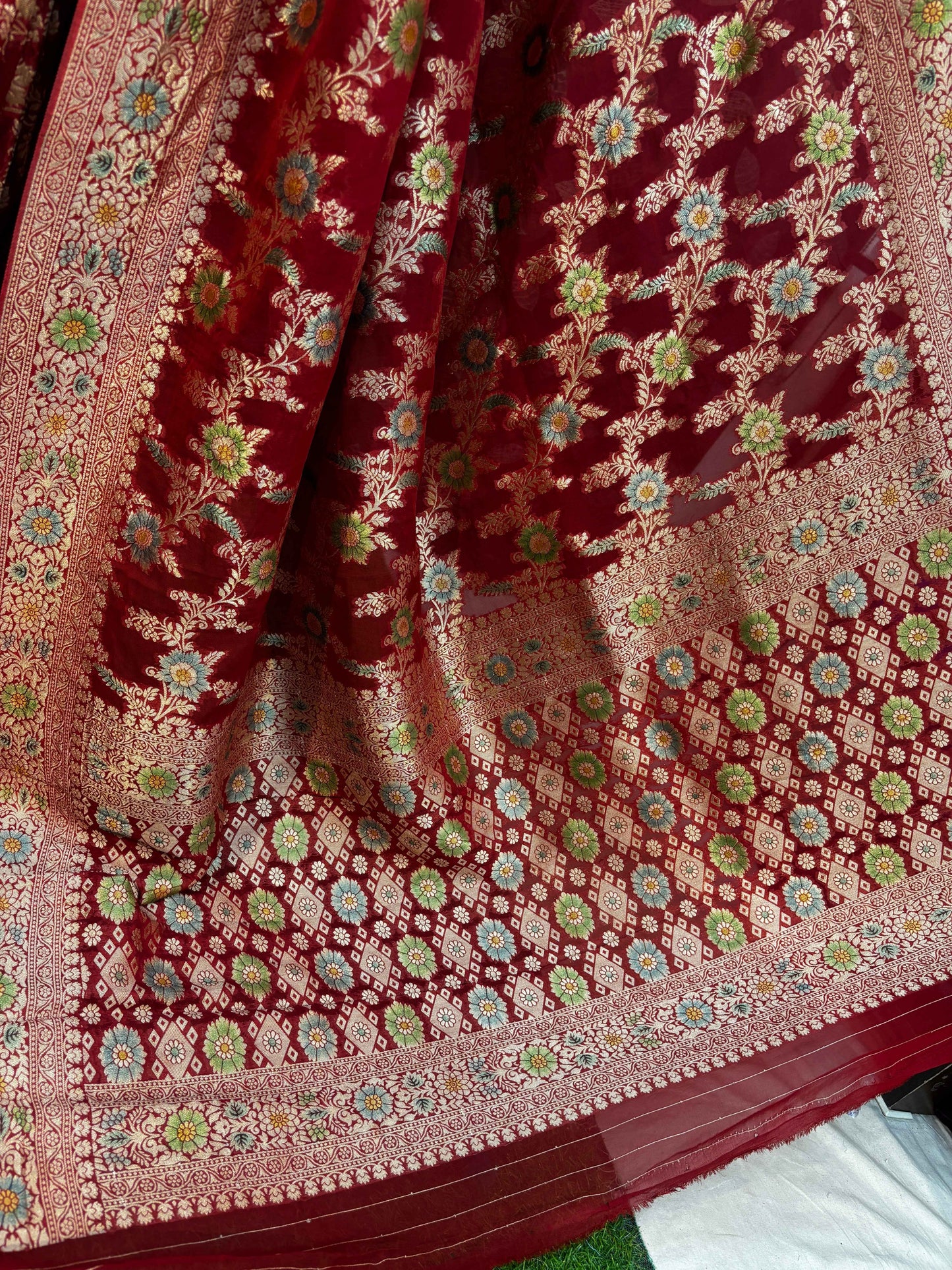 Red Banarasi georgette saree with detailed floral motifs and cream-gold border, close-up fabric.