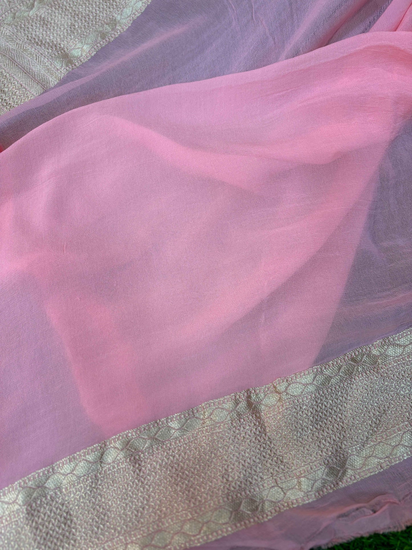 Sheer light pink saree pallu with subtle woven texture and gold zari edge