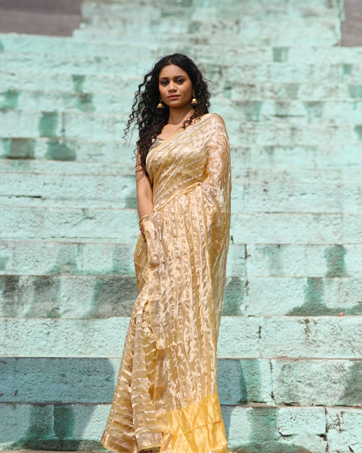 Gold Banarasi tissue handloom saree with shimmering zari motifs, draped over one shoulder.