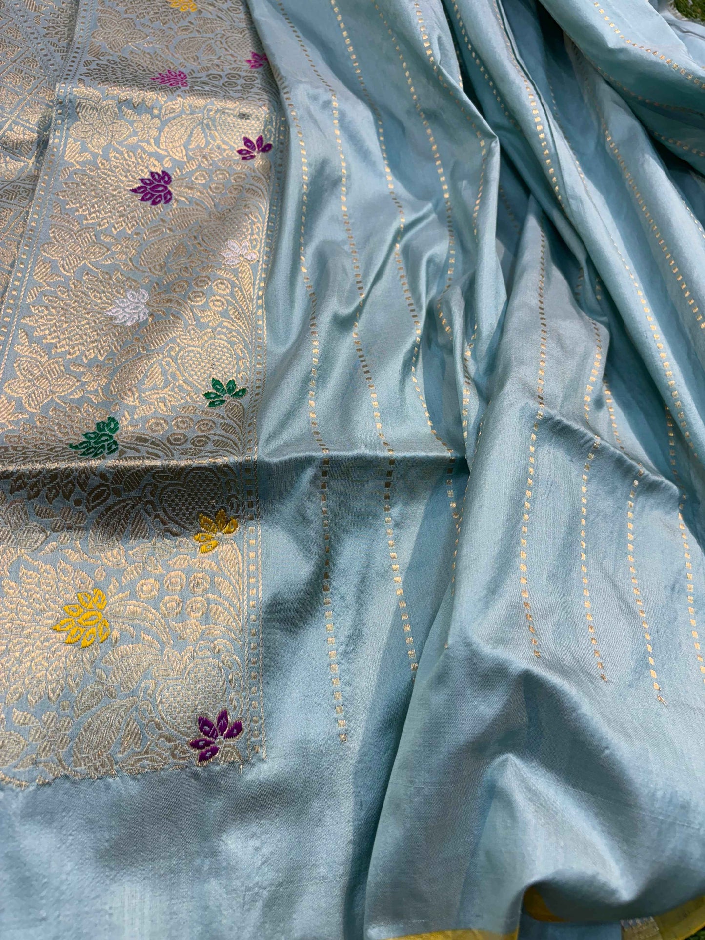Light blue saree fabric with silver zari sheen and small multicolor floral motifs throughout.