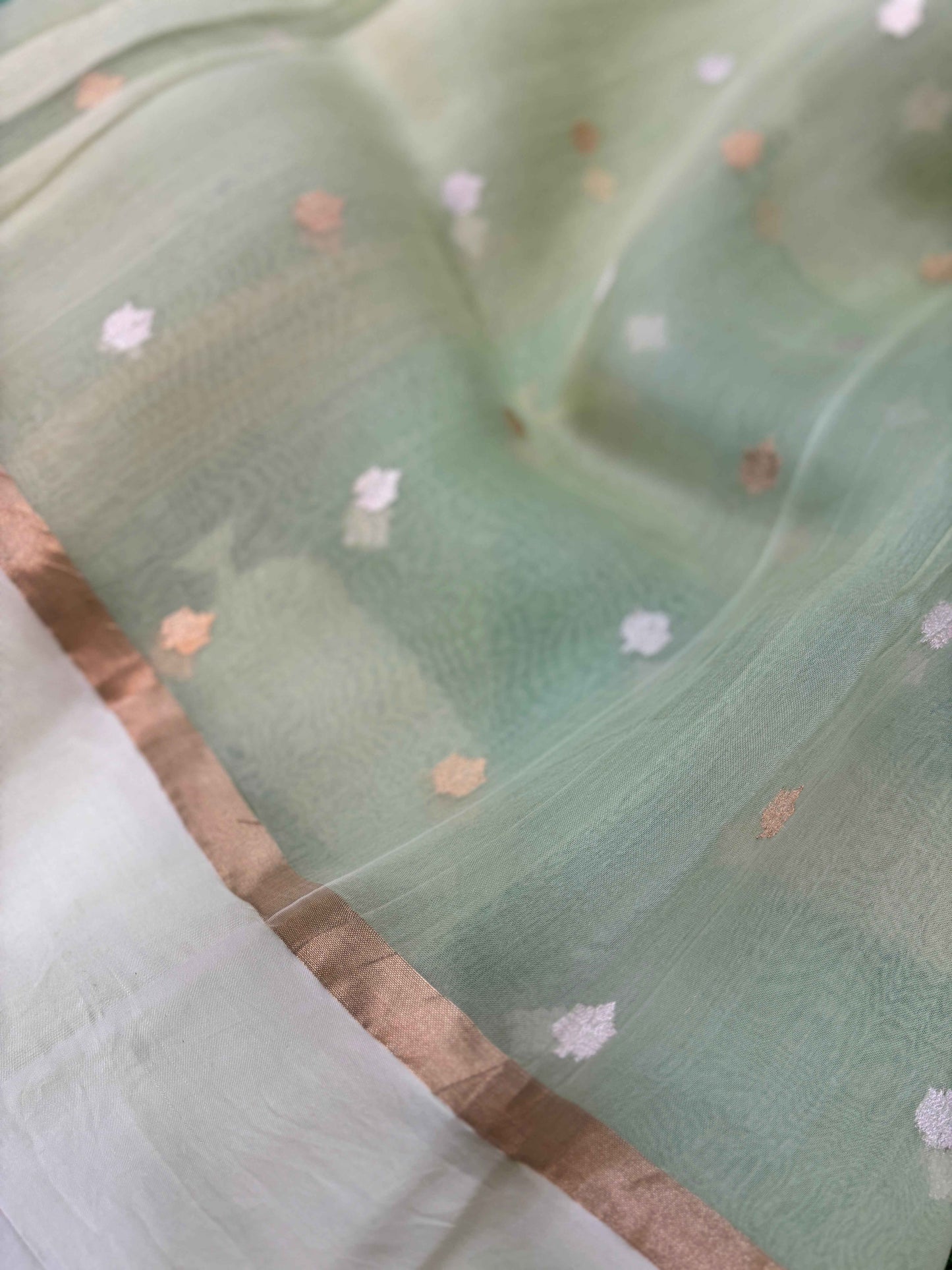 Aqua saree close-up with tiny floral sprigs and thin bronze-gold border edge