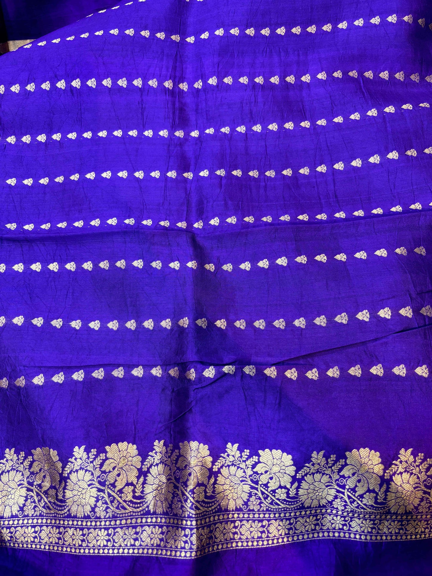 Purple saree fabric close-up with repeating gold stripe bands and ornate border