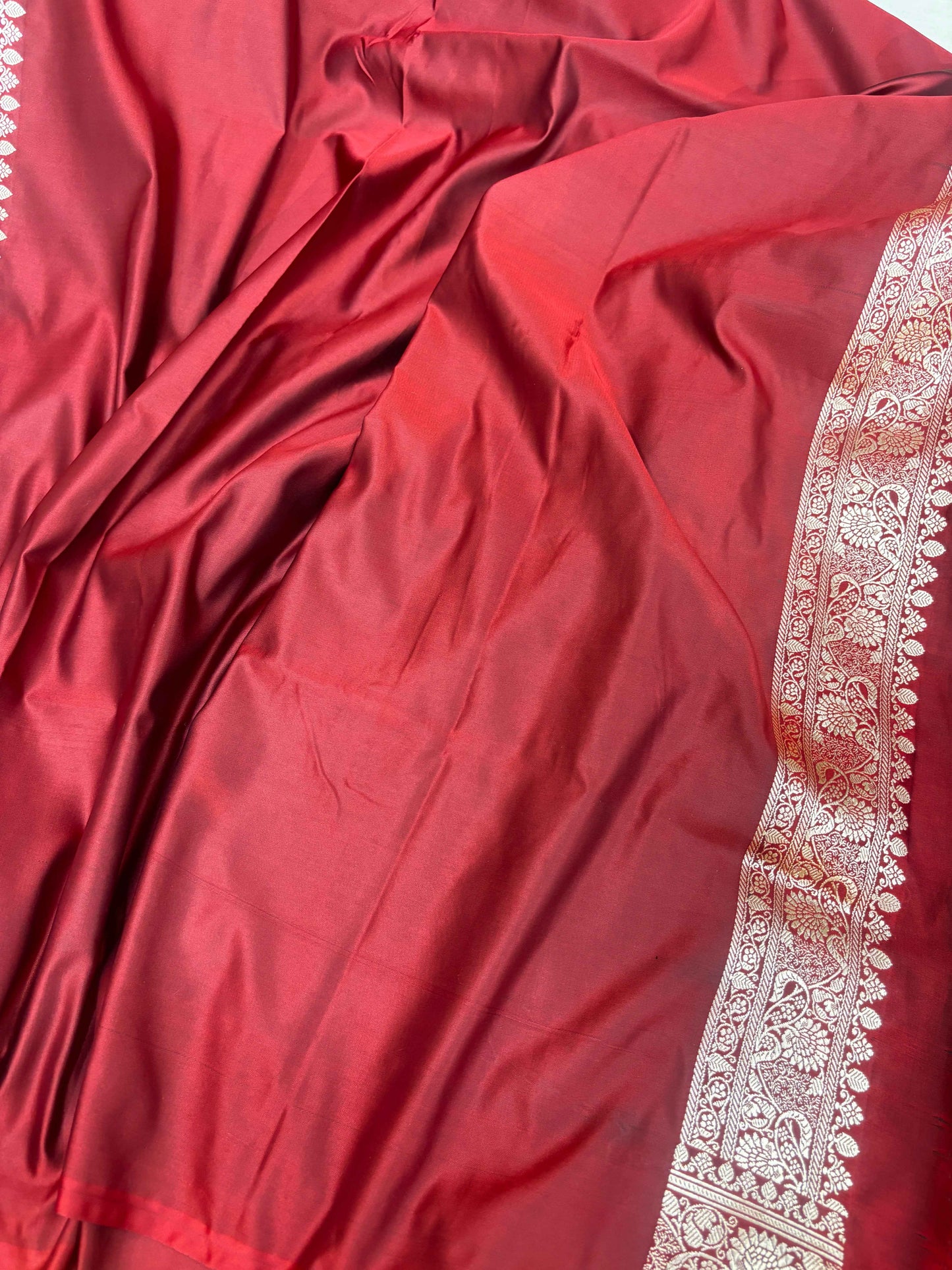 Maroon silk saree fabric with subtle sheen and cream-gold embroidered border edge