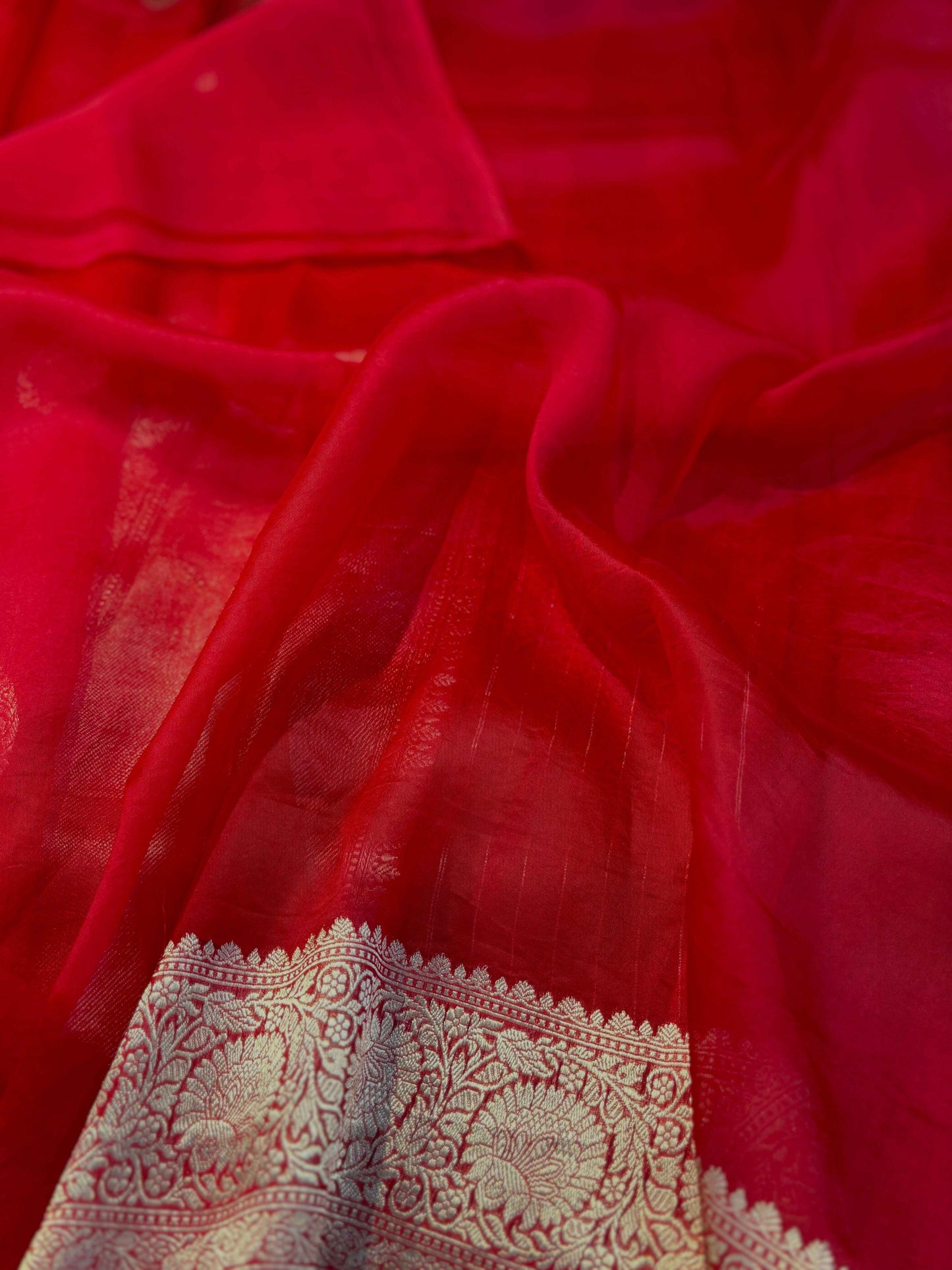 Red silk saree close-up with ornate silver zari border band at hem