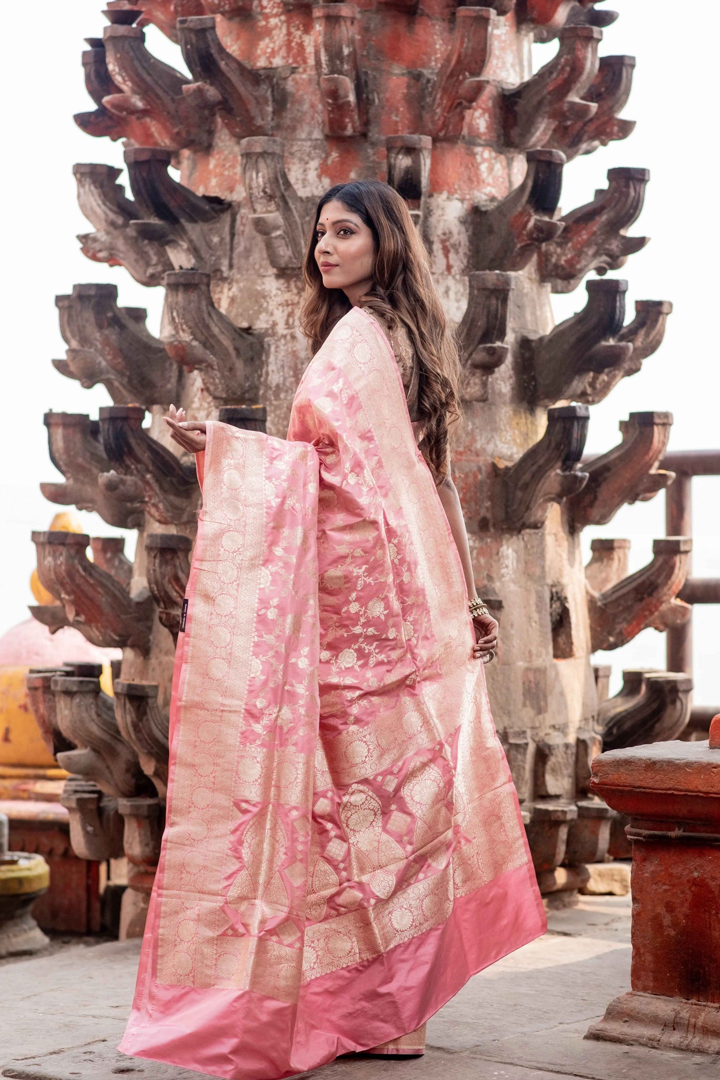 Pink saree with gold-toned woven border and cutwork motifs, draped in profile.