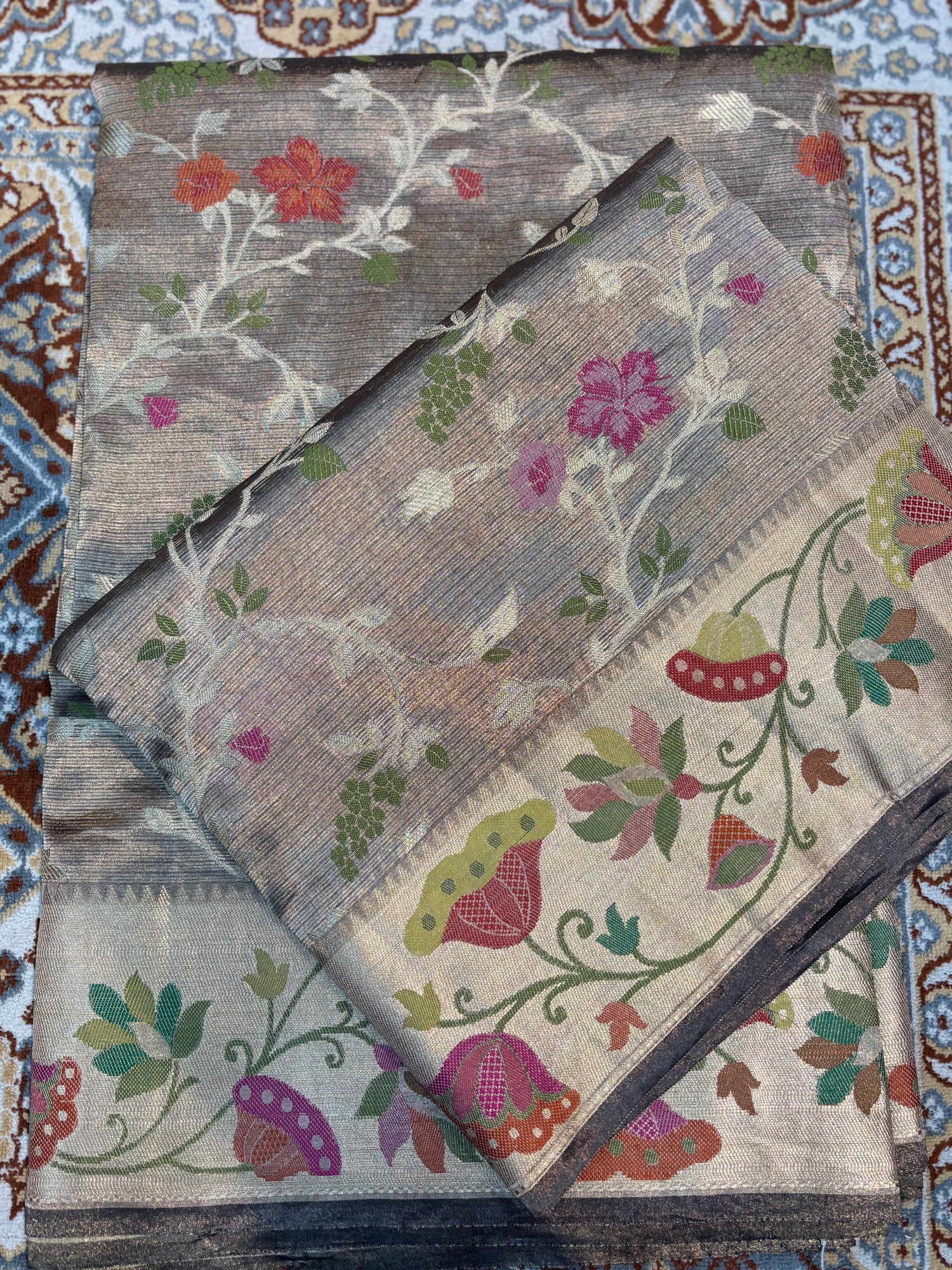 Silver-grey saree with floral and bird prints and dark border across folded fabric