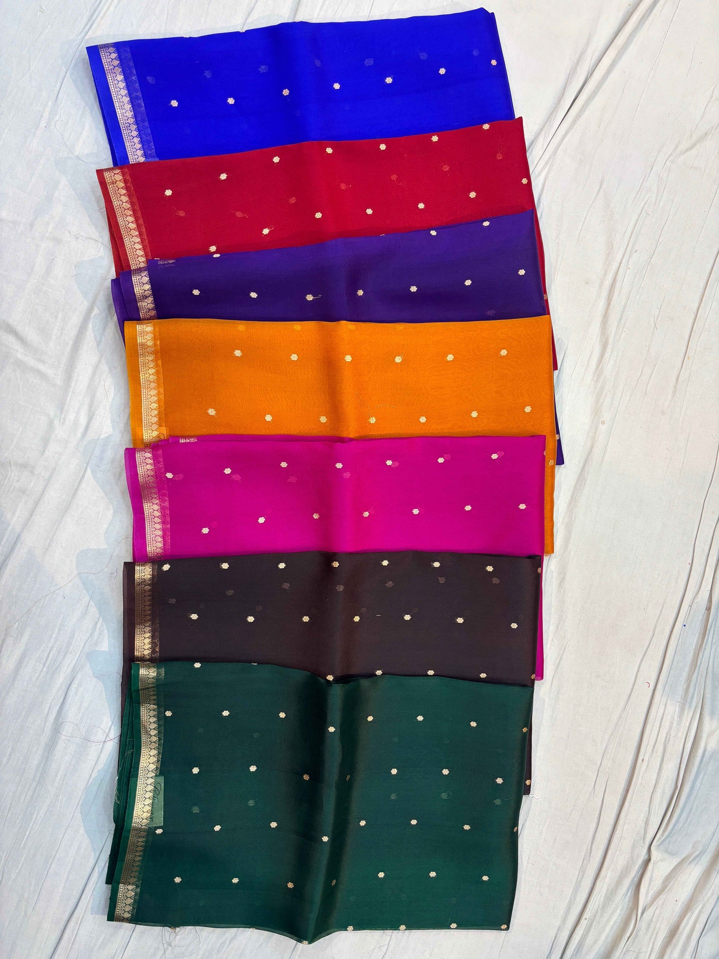 Multicolor Banarasi handloom sarees with gold borders and dotted motifs, folded