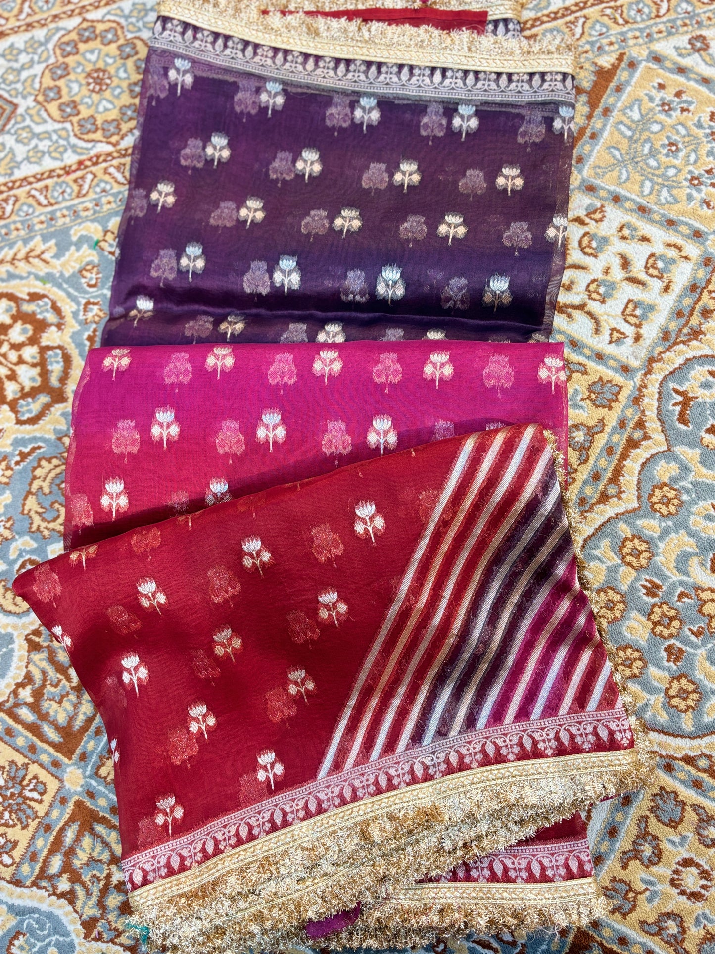Folded saree pieces with purple and maroon motifs, striped panel, and gold border