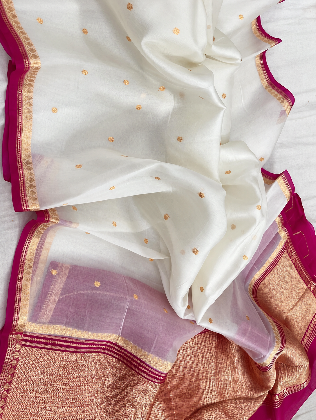 White silk saree fabric close-up with gold speckled motifs and pink border