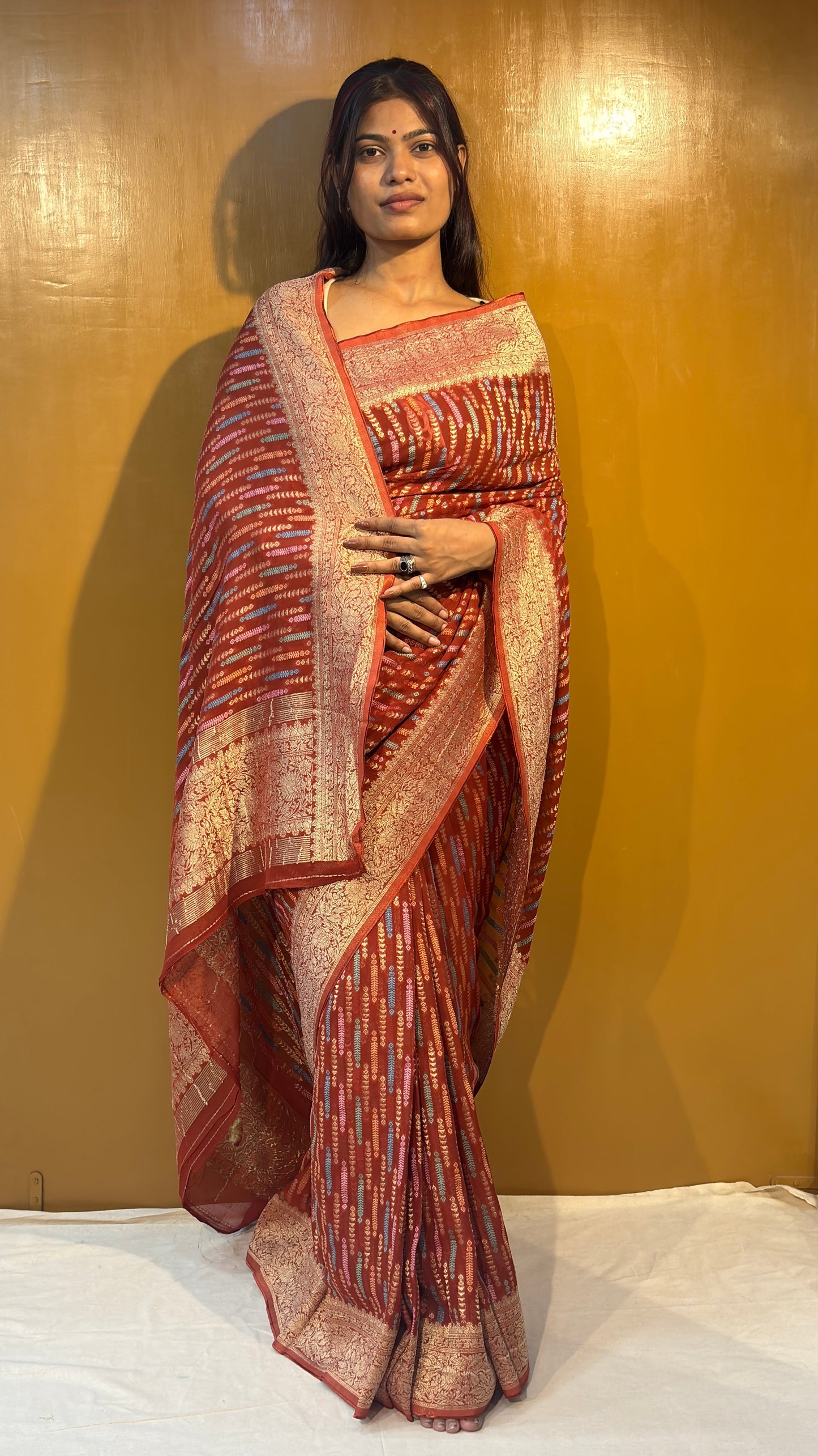 Pink saree with gold-toned pattern and ornate cream border, pallu across front