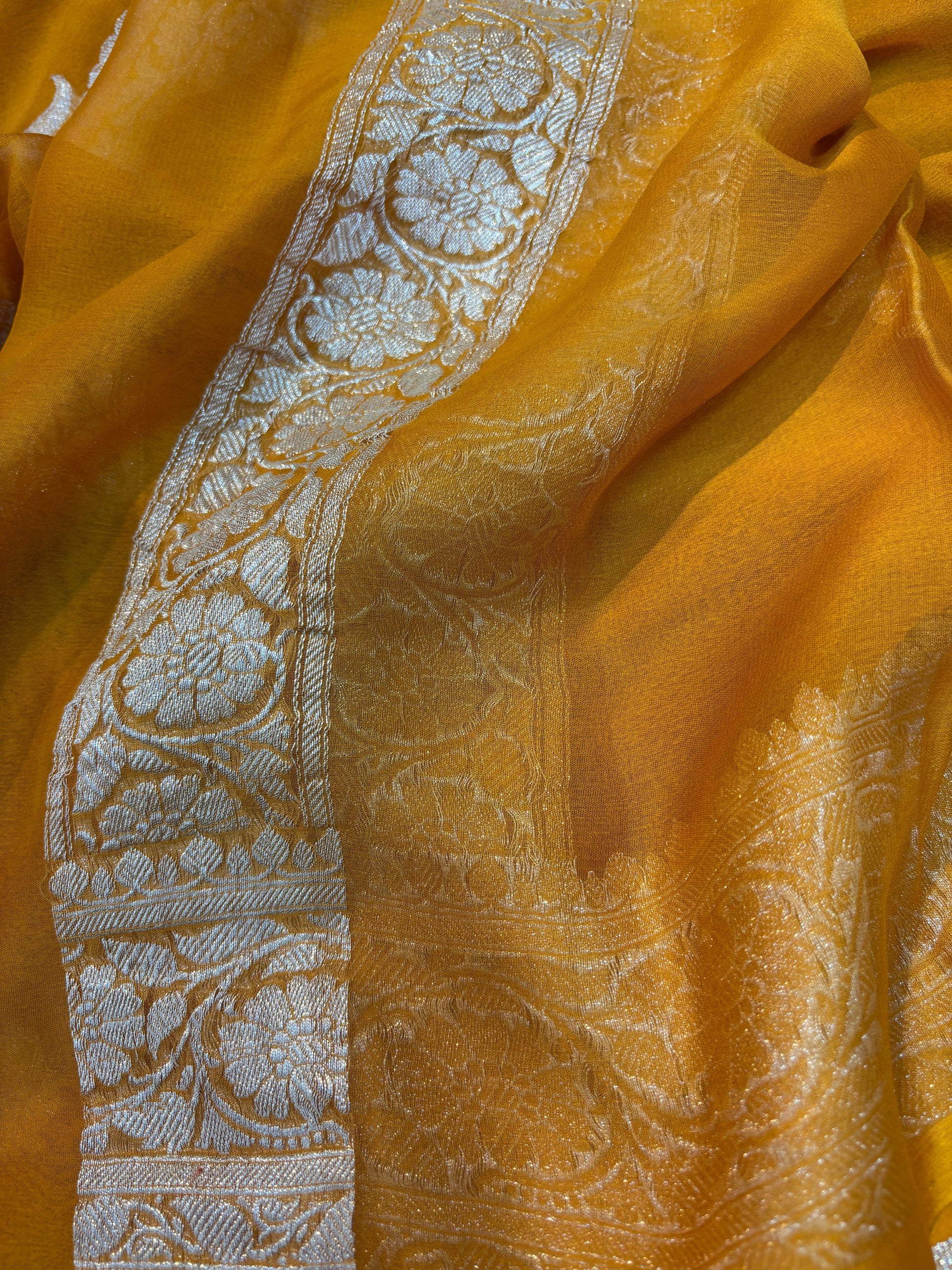 Mustard yellow Banarasi handloom saree with silver-tone embroidered border and floral strip.