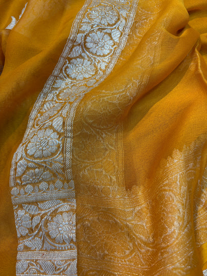 Mustard yellow Banarasi handloom saree with silver-tone embroidered border and floral strip.