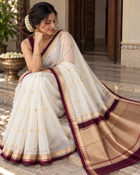 Woman wearing ivory silk saree with gold motifs and maroon-gold wide border