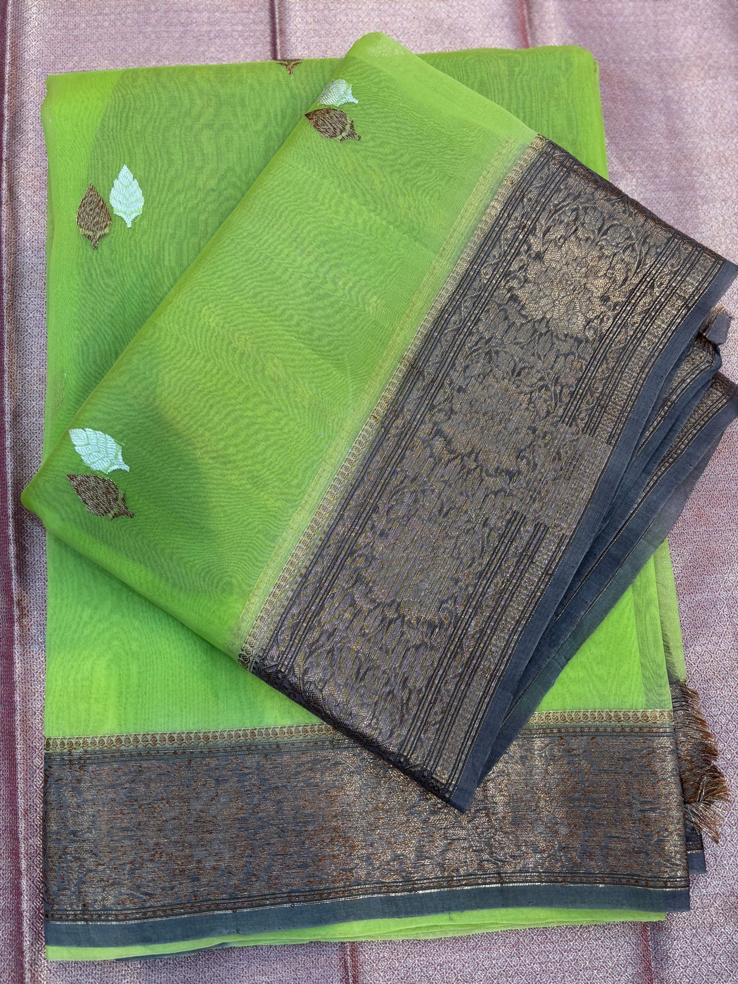 Folded green silk saree with leaf motifs and dark patterned zari-style border