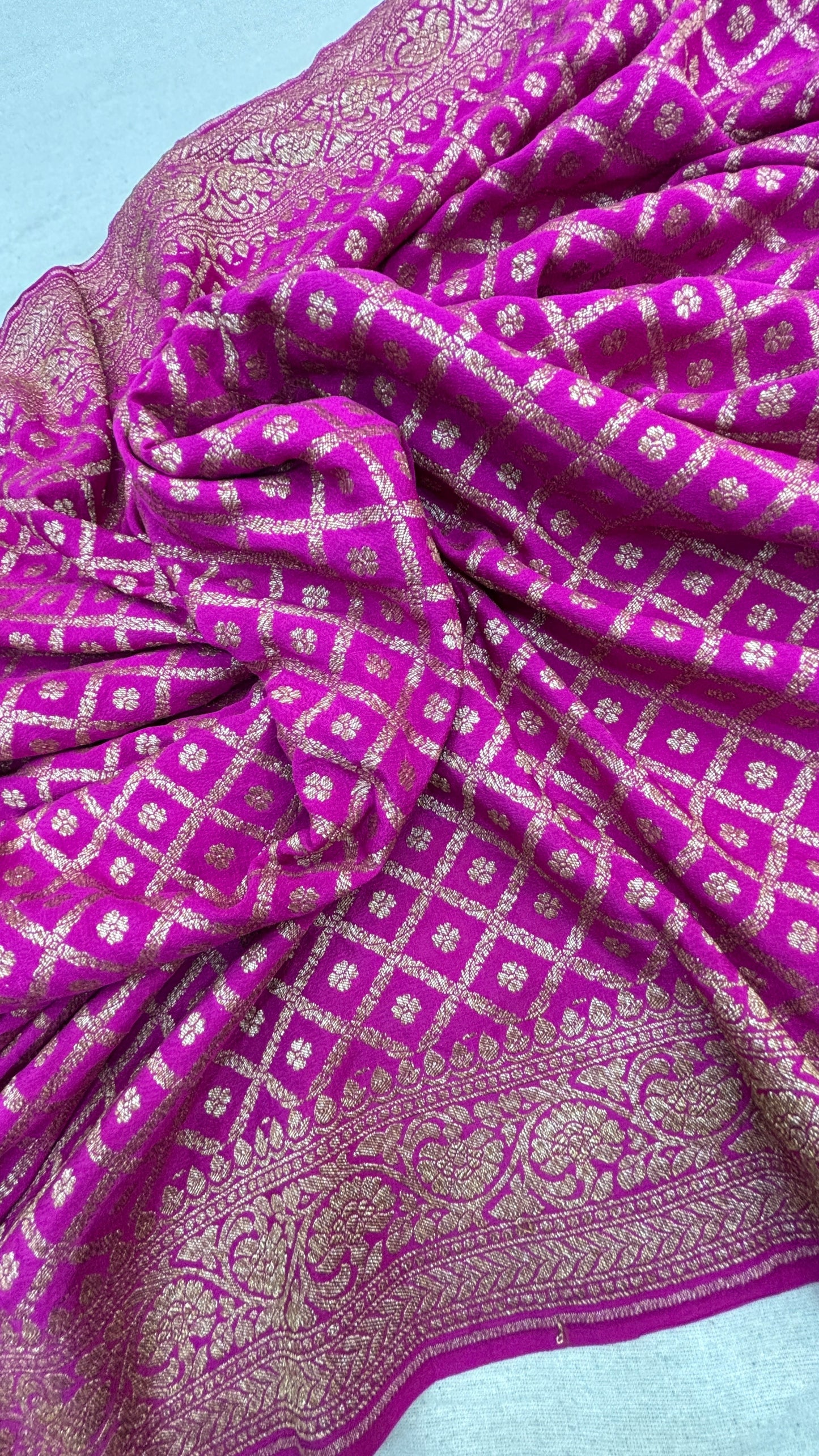 Rani pink saree fabric close-up with gold motifs and ornate zari border