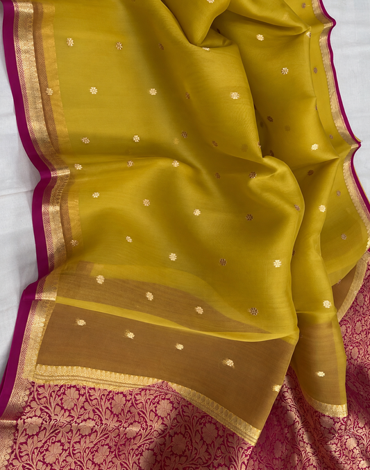 Green silk saree fabric close-up with gold zari border, small dot motifs and magenta edge
