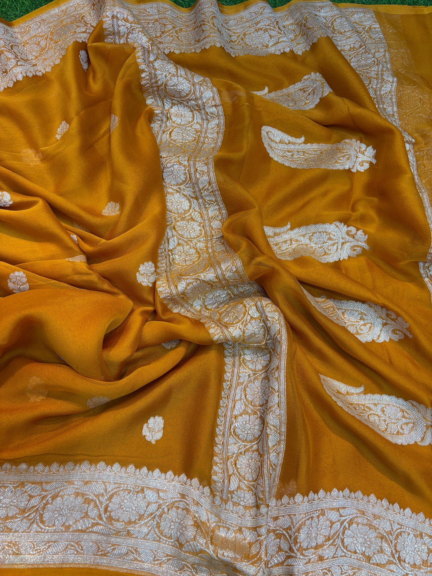 Mustard yellow Banarasi handloom saree with silver-tone motifs and patterned border.